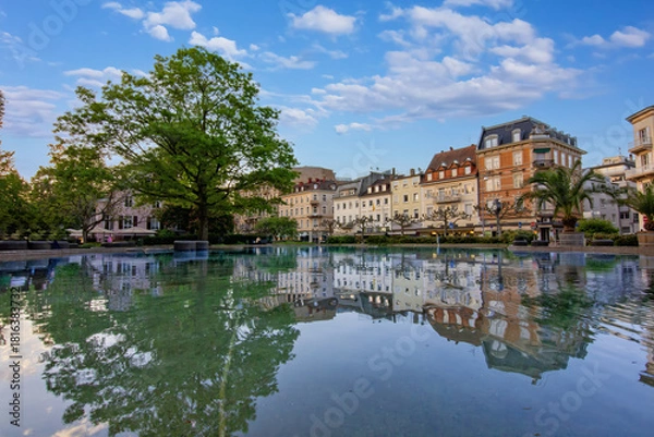 Fototapeta Augustaplatz in Baden-Baden, dominated by the large, glassy surface of a fountain or decorative pond in the foreground