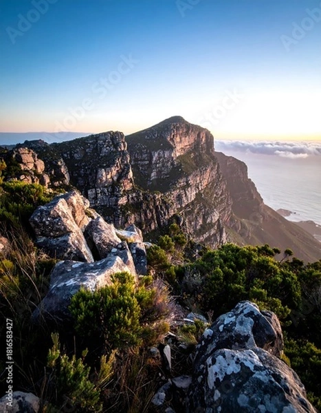 Fototapeta A breathtaking perspective of a rugged mountain vista under a clear, cloud-kissed sky during the golden hour, with the sea visible