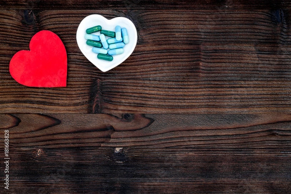 Obraz Treat heart. Pills in bowl in shape of heart near stethoscope on dark wooden background top view copyspace