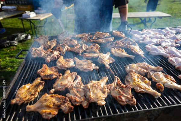 Fototapeta Shallow depth of field (selective focus) details with chicken thighs on a metal barbecue outdoors during a sunny day