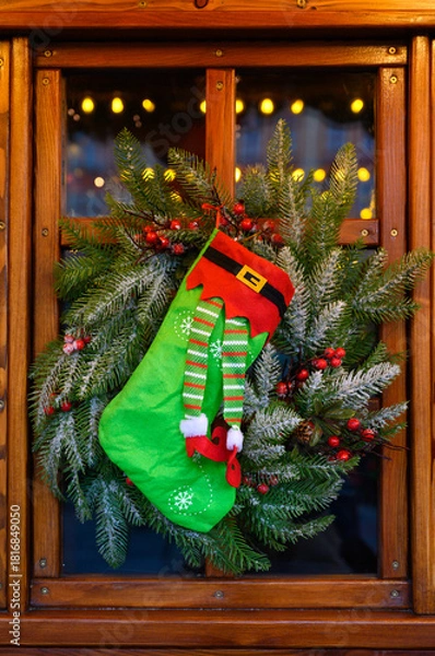 Fototapeta A cozy Christmas stocking displayed on a rustic window frame with greenery, ornaments, and glowing lights. Ideal for promotions, home decor brands, festive marketing materials, and Christmas designs.