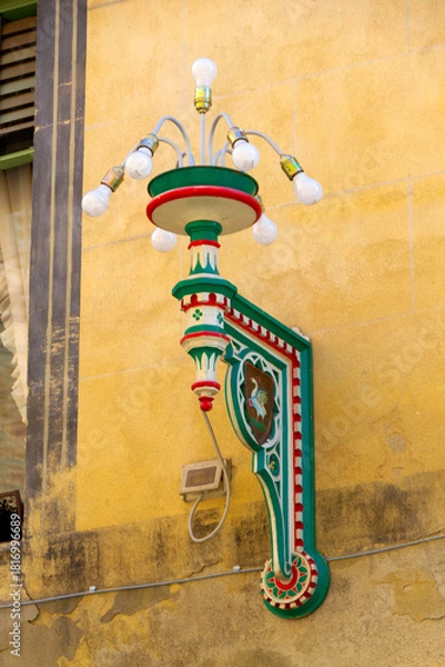 Obraz Colorful Ornate Street Lamp With Green Red Details Mounted on Yellow Stucco Wall Historic Facade