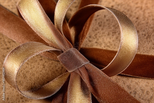 Fototapeta Elegant brown and gold ribbon bow for festive gift wrapping on textured background