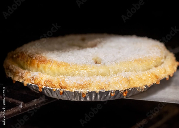 Fototapeta Close-up of a rustic, raw dough cherry pie, glistening with a sugar topping, being slid into a hot dark oven to begin baking in the cafe.