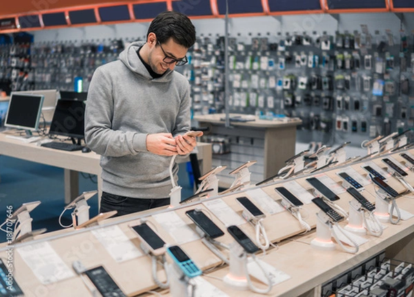Fototapeta Happy male customer choosing smartphone in the mobile phone shop. difficult decision. Various choice. He is smiling