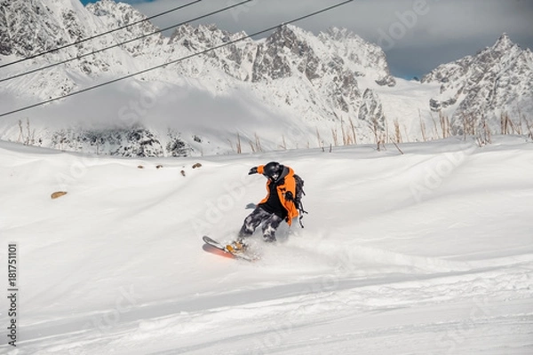 Fototapeta Snowboarder in colorful sportswear riding on the snow hill