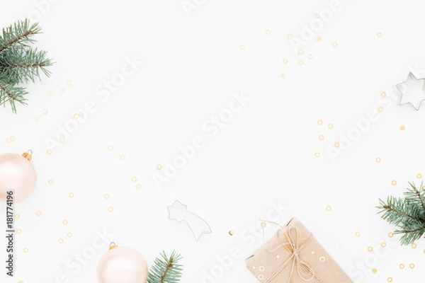 Fototapeta Minimal styled Christmas background with gift box, blush baubles, fir branches and baking molds on white. Holiday flat lay, top view.