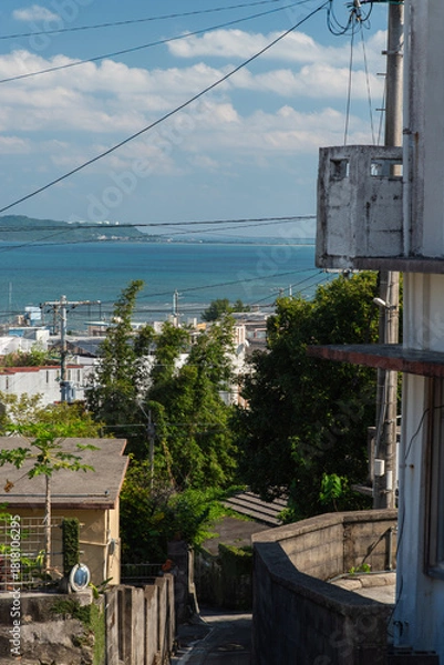 Obraz 快晴の空とエメラルドグリーンの海の見える街並みと下り坂