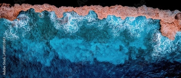 Fototapeta An aerial drone shot captures the vibrant turquoise ocean meeting a rugged, sandy coastline with white foam from crashing waves.