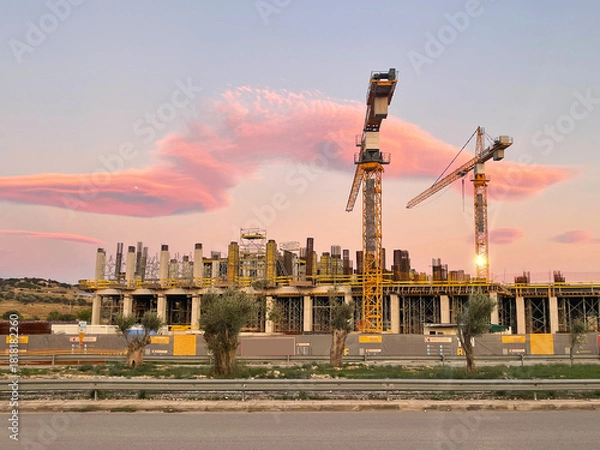Obraz A modern construction site with tall cranes at sunset. Industrial building, urban development, architecture, and progress. City street, construction in progress. Athens, Greece.
