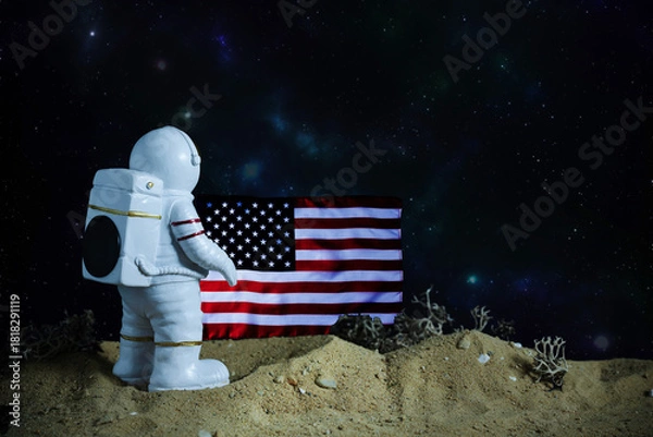 Fototapeta Astronaut toy on rough sand that looks like lunar ground, USA flag beside, representing outer space mission and discovery.