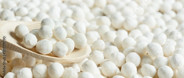 Obraz White dry tapioca pearls in wooden spoon on tapioca background. Raw tapioca starch balls used for bubble tea or desserts. Tapioca pearls as healthy gluten free ingredient.