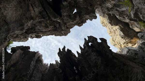 Fototapeta A view of the blue sky from a deep pit with sharp rocks