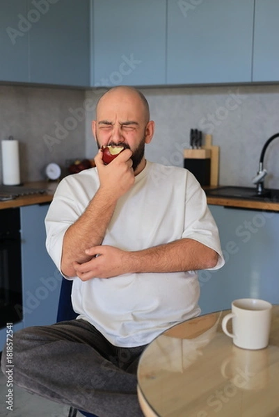 Obraz Man reacting strongly while biting into an apple, expressing an unpleasant or surprising taste during a real emotional moment in the kitchen