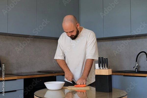 Obraz Man chopping carrots in the kitchen with a focused, neutral expression during a calm home cooking moment