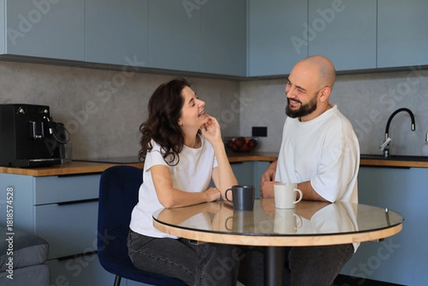 Obraz Couple smiling and talking at the kitchen table, enjoying a pleasant conversation and relaxed moment together in a cozy home environment
