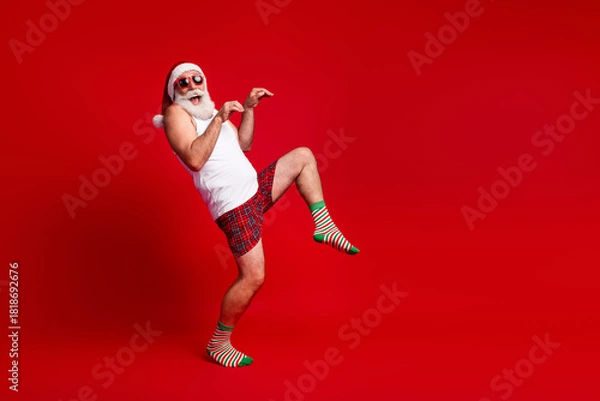 Obraz Playful Santa look alike dances in bright red studio wearing white tank top plaid shorts and striped socks for festive christmas vibe