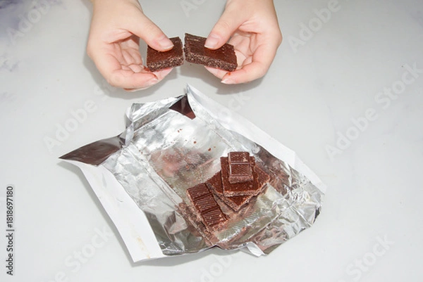 Obraz  A broken bar of chocolate in girlish hands against the background of chocolate lying in an unfolded foil.