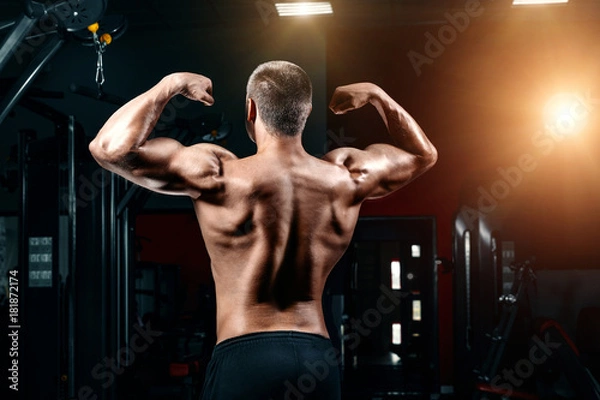 Fototapeta Young Man Standing Strong In The Gym And Flexing Muscles - Muscular Athletic Bodybuilder Fitness Model Posing After Exercises