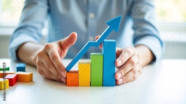 Fototapeta A person arranging colorful wooden blocks into a bar graph with a blue upward arrow, symbolizing business growth or progress.