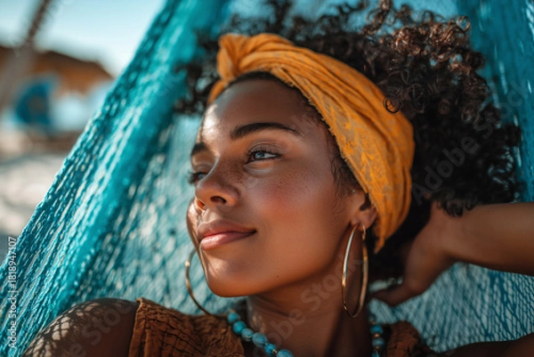 Fototapeta A young African American woman lounging on the beach, relaxing in a hammock with her hands resting behind her head.