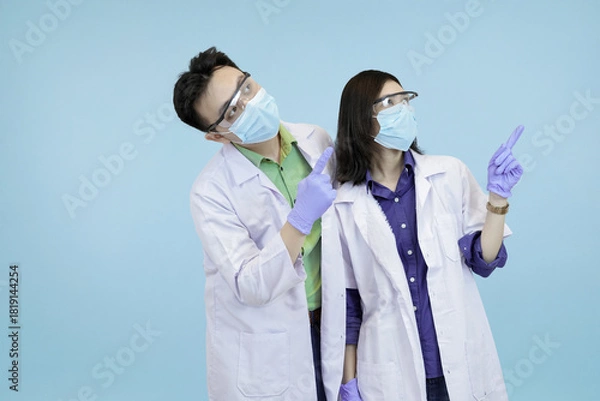 Fototapeta Asian medical pointing upwards, signifying instruction, attention, or a new successful direction in blue studio background