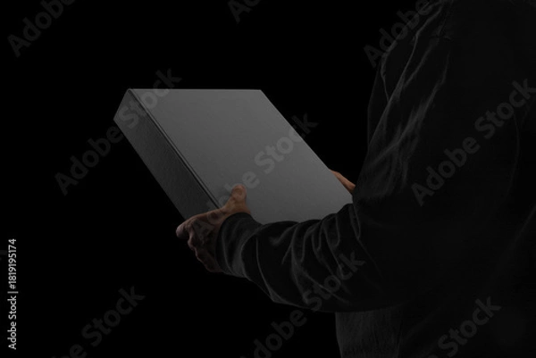 Obraz A closed binder box held by a person wearing dark clothing. Minimalistic blackout style with moody, low-key lighting. Perfect for showcasing packaging, premium stationery, branding concepts
