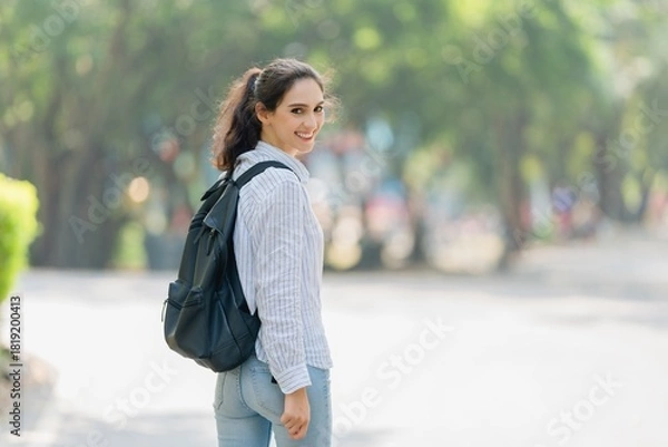 Fototapeta Smiling young professional woman turning back on a path, confident invitation, welcome, and the start of a new journey