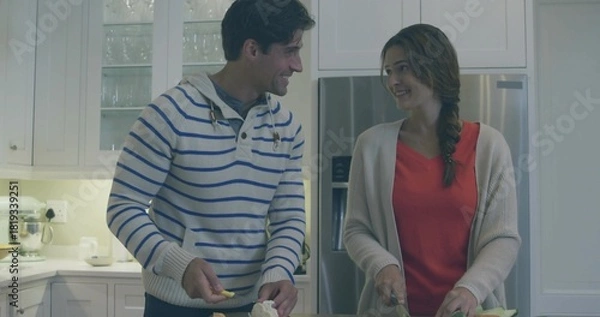 Obraz Chopping couple wearing red top and striped sweater locking eyes at kitchen island, using knives