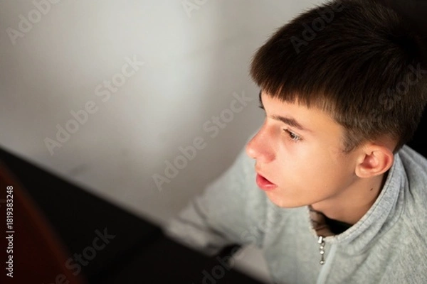Fototapeta Deep in thought, a teenager contemplates ideas while seated at a table in a cozy, minimalist room during the soft afternoon light
