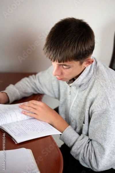 Fototapeta Focused student engaged in studying diligently at a wooden desk in a bright room during the late afternoon, demonstrating the essence of learning and dedication to education