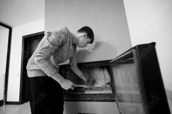 Fototapeta Man engaged in cleaning a fireplace in a cozy living room setting during a tranquil morning, showcasing dedication to home upkeep and personal space enhancement