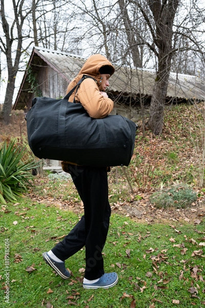 Fototapeta Carrying a large duffel bag through a quiet autumn landscape in the countryside while dressed warmly against the chill of early morning