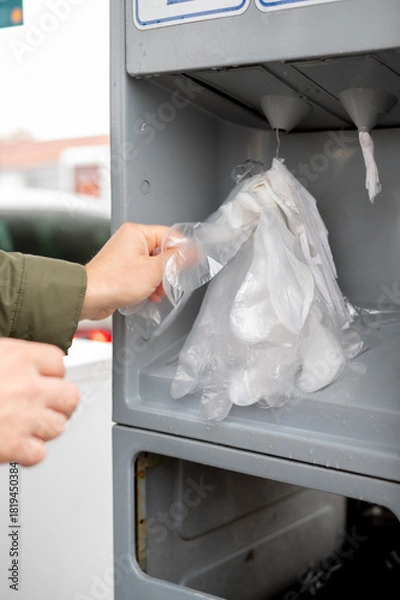 Fototapeta A man at a gas station takes disposable plastic gloves before refueling his car, showing attention to cleanliness, hygiene, and preparation for safe handling of fuel
