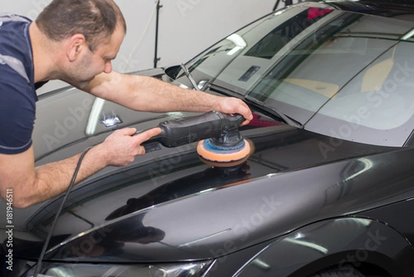 Obraz A man polishes a black car with a polisher