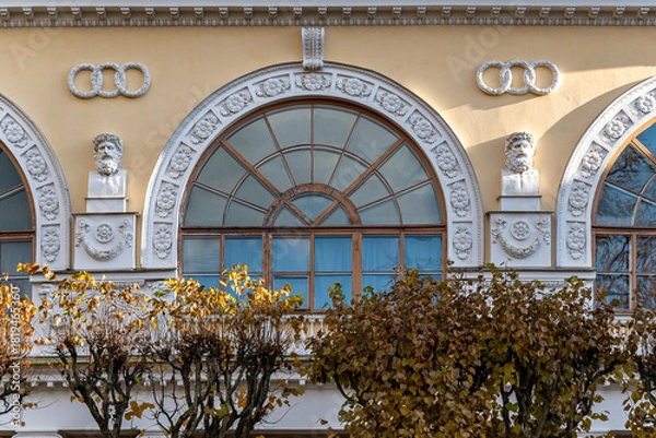 Fototapeta Large arched window against a yellow wall with a bas-relief and white sculptures arranged symmetrically on both sides. From the Mira window series.