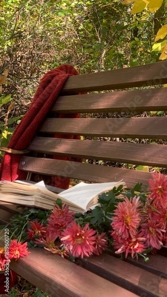 Fototapeta Cozy autumn reading spot with a blanket, a book, and blooming flowers in a serene natural setting