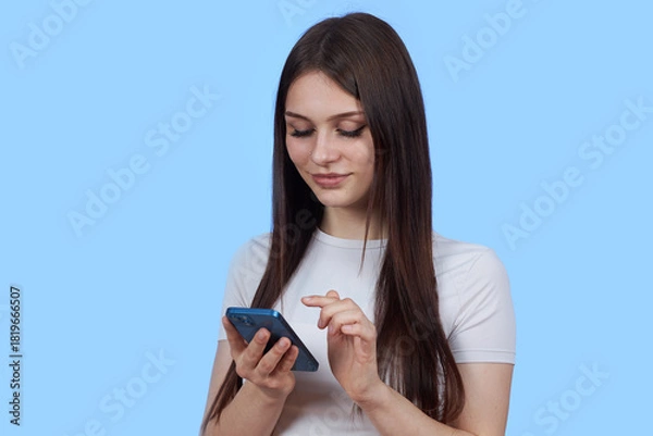 Obraz A young attractive female student uses a mobile phone. The figure is isolated on a blue background.