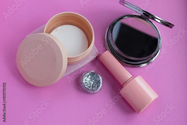 Fototapeta Beauty products and makeup accessories for self care routine, featuring pink nail polish, glitter, compact mirror, and face powder on a vibrant pink background