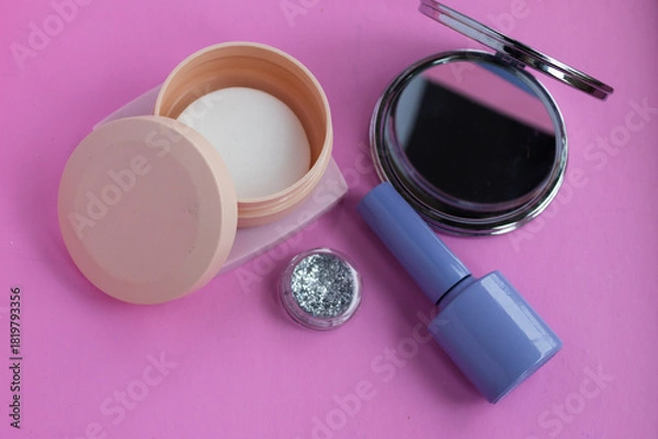 Fototapeta Cosmetics arrangement on a vibrant pink background featuring a compact mirror, loose glitter, a container of nail polish remover wipes, and nail polish, symbolizing beauty and self care