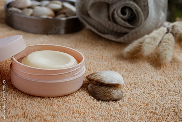 Fototapeta Open container of nourishing moisturizing cream for skincare routine during a relaxing spa and wellness treatment with seashells and soft towels, promoting beauty and self care