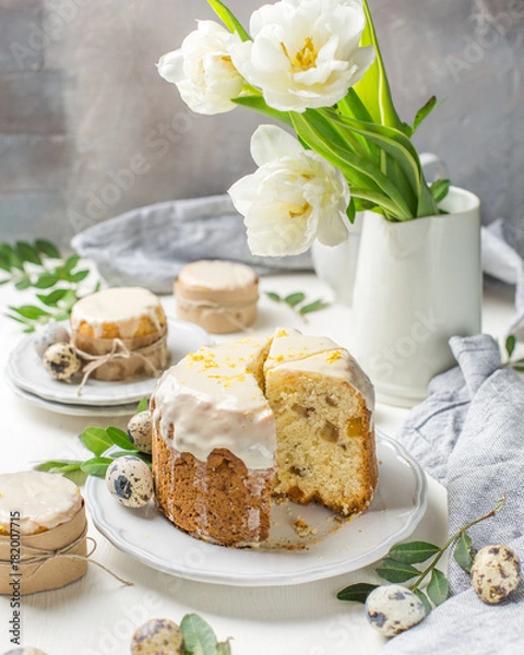 Obraz Traditional Easter cake on a light wooden background. Decorated with flowers. Next to a small cake, quail eggs and flowers. Cut a piece of cake. Easter. Celebration. Spring. Rustic style