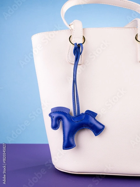 Obraz Close-up of a fashionable blue leather horse keychain with a saddle, attached to a white stylish bag