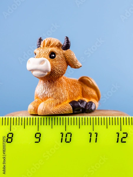 Obraz Close-up of a small, cute figurine in the shape of a brown cow, placed on a wooden podium.
