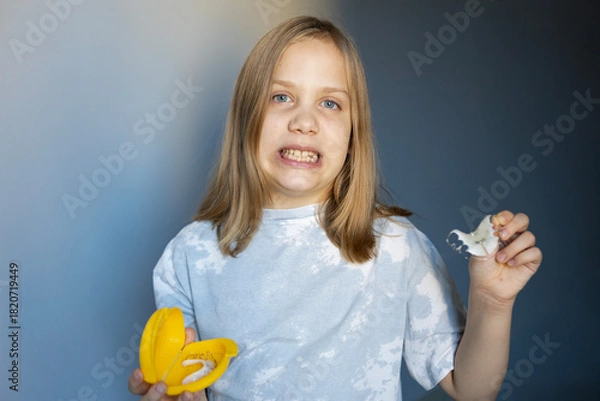 Fototapeta Young child holding a banana peeler and a banana peel with a confused expression at home during daytime