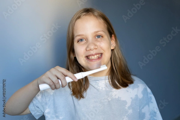 Fototapeta Girl smiles while brushing teeth in a well-lit room during morning routine