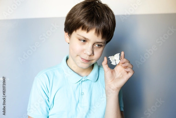 Fototapeta Boy smiles while holding a small piece of paper with a shape in a blue and white room