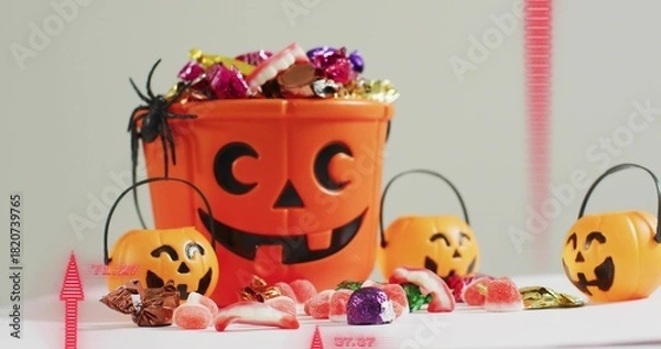 Obraz Showing orange pumpkin bucket spilling wrapped candies beside three pails on white table, spider
