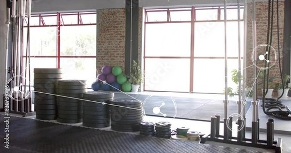 Fototapeta Stacking black bumper plates occupying left-of-center on rubber floor, with colorful balls