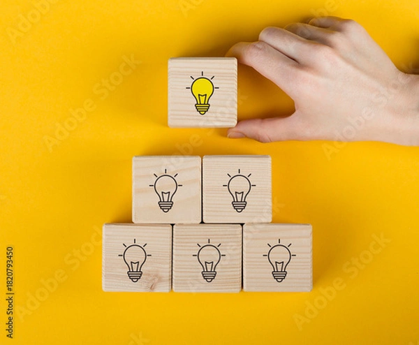 Fototapeta Creative idea, solution and innovation concept. Idea generation and screening for product development process. Wooden blocks with light bulb and yellow color icons on clean background and copy space